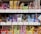 A variety of packaged snacks and treats are neatly displayed on grocery store shelves. The packaging features vibrant colors such as red, yellow, and blue, with labels in Japanese text. Each row on the shelves showcases different types of snacks, including both sweet and savory options.