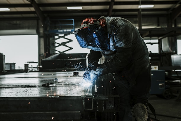 Skilled welder working with sparks flying in a controlled industrial workshop.