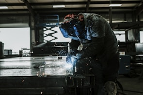 Technicians welding metal structures wearing protective gear in a controlled industrial environment.