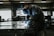 A welder wearing protective gear is working on a metal piece in a dimly lit industrial workshop. Sparks fly from the welding torch, casting light on the surrounding area.