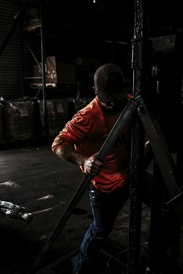 A worker wearing safety gear confidently checking industrial equipment in a bright warehouse.