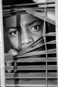 grayscale photo of person holding window blinds