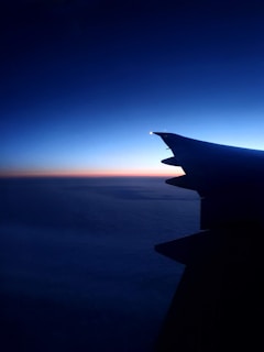 A sleek plane soaring against a vibrant gradient sky transitioning from day to sunset.