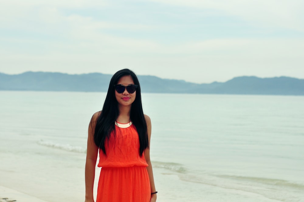 mulher no vestido alaranjado sem mangas que está na praia durante o dia