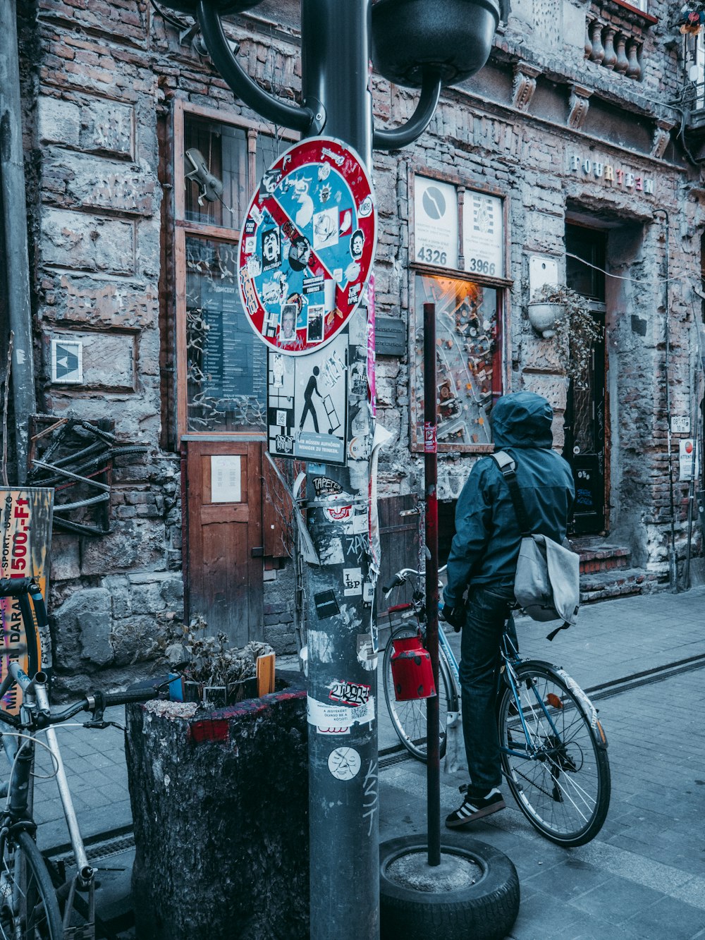 man in black jacket and blue denim jeans standing beside bicycle during daytime