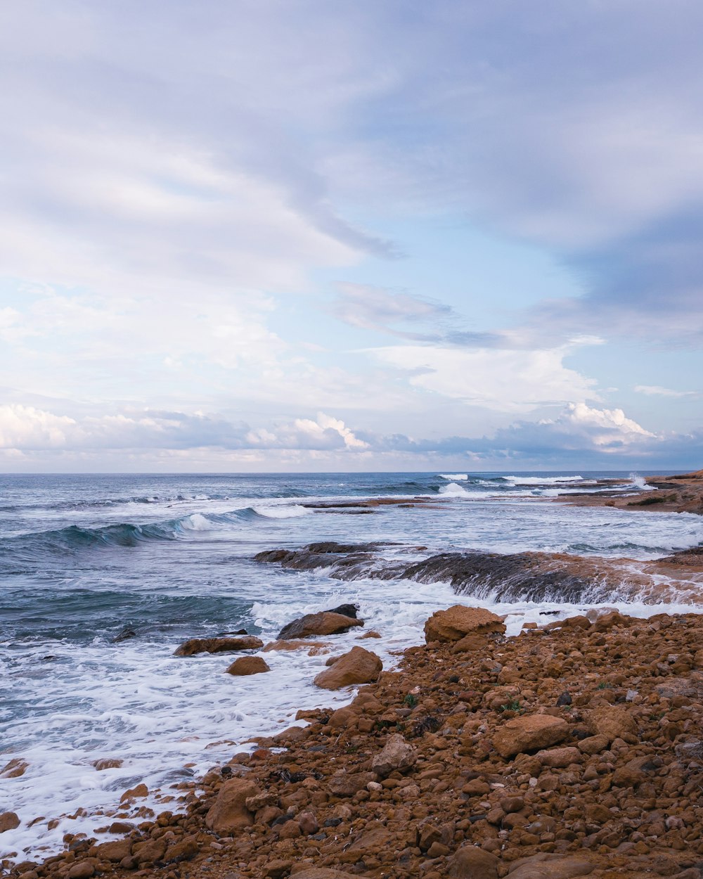 ocean waves crashing on rocks under white clouds and blue sky during daytime