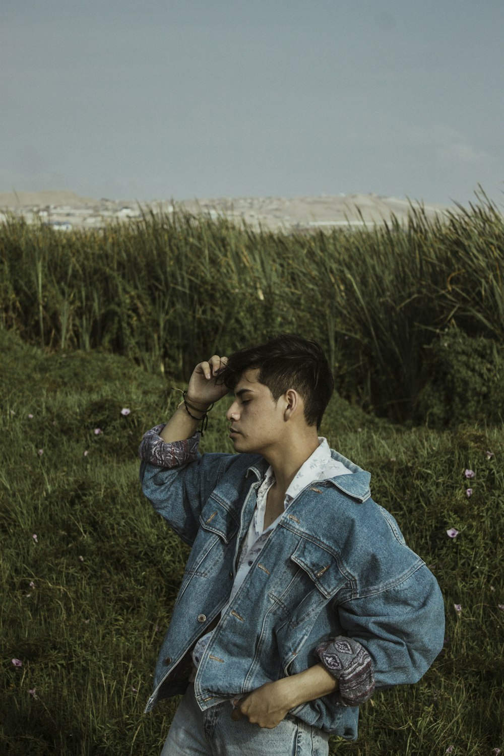 man in blue denim jacket standing on green grass field during daytime