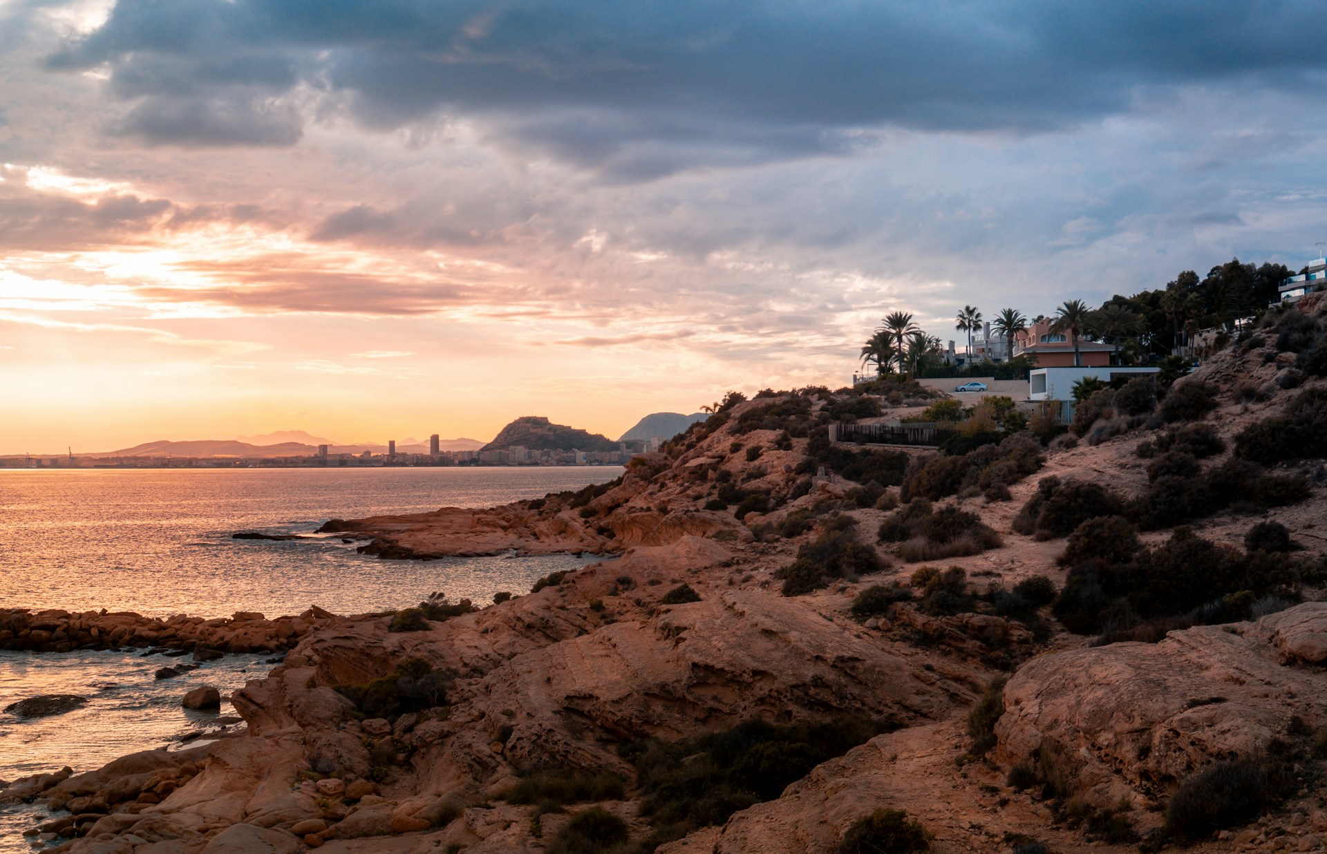 white and brown concrete building on brown rocky shore under white clouds during daytime