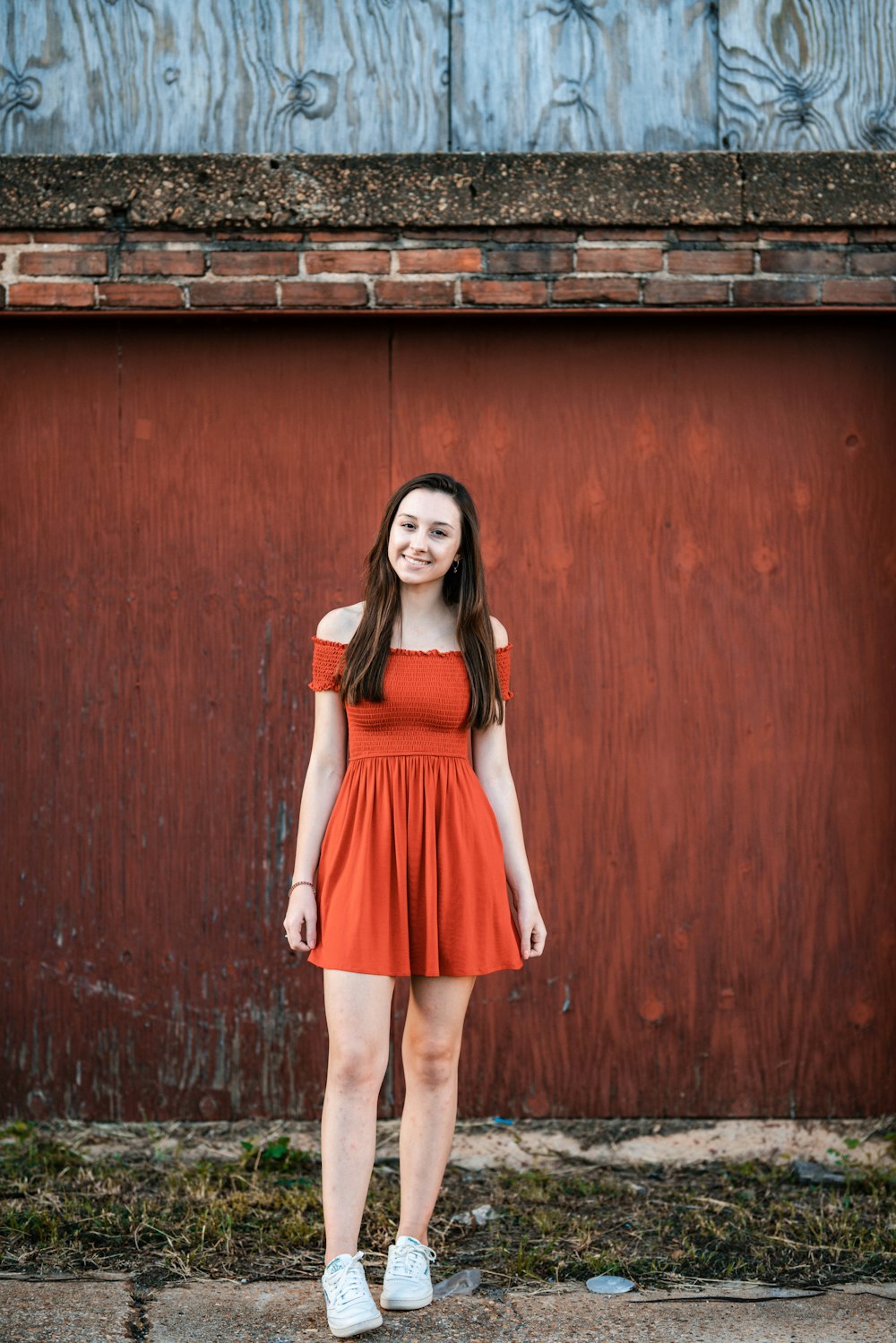 woman in red sleeveless dress standing beside brown wooden wall