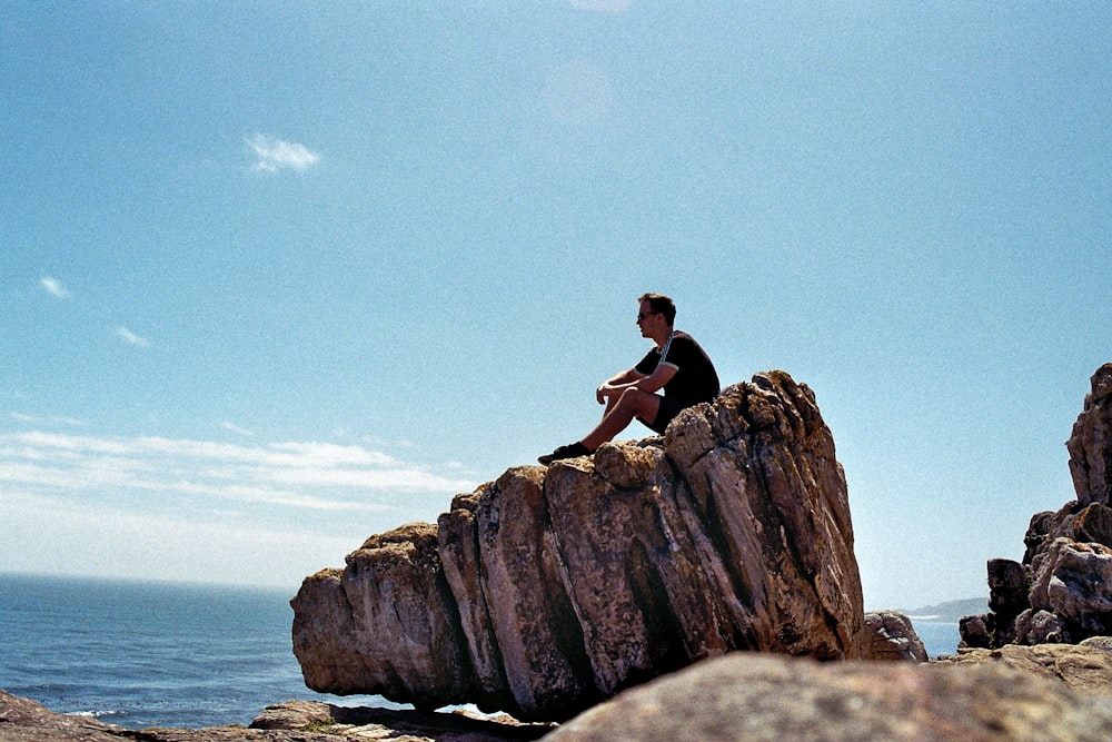 woman in black tank top sitting on brown rock formation during daytime