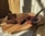 A rustic wooden board holding a loaf of freshly baked chocolate cake, partly sliced, sitting on parchment paper. Beside it is a glass bowl filled with a rich red berry sauce and a whisk resting inside.