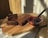 A rustic wooden board holding a loaf of freshly baked chocolate cake, partly sliced, sitting on parchment paper. Beside it is a glass bowl filled with a rich red berry sauce and a whisk resting inside.