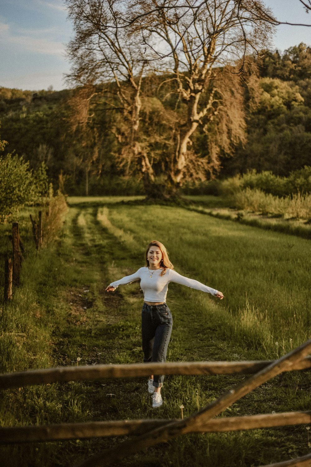 girl in white long sleeve shirt and blue denim jeans standing on brown wooden fence during