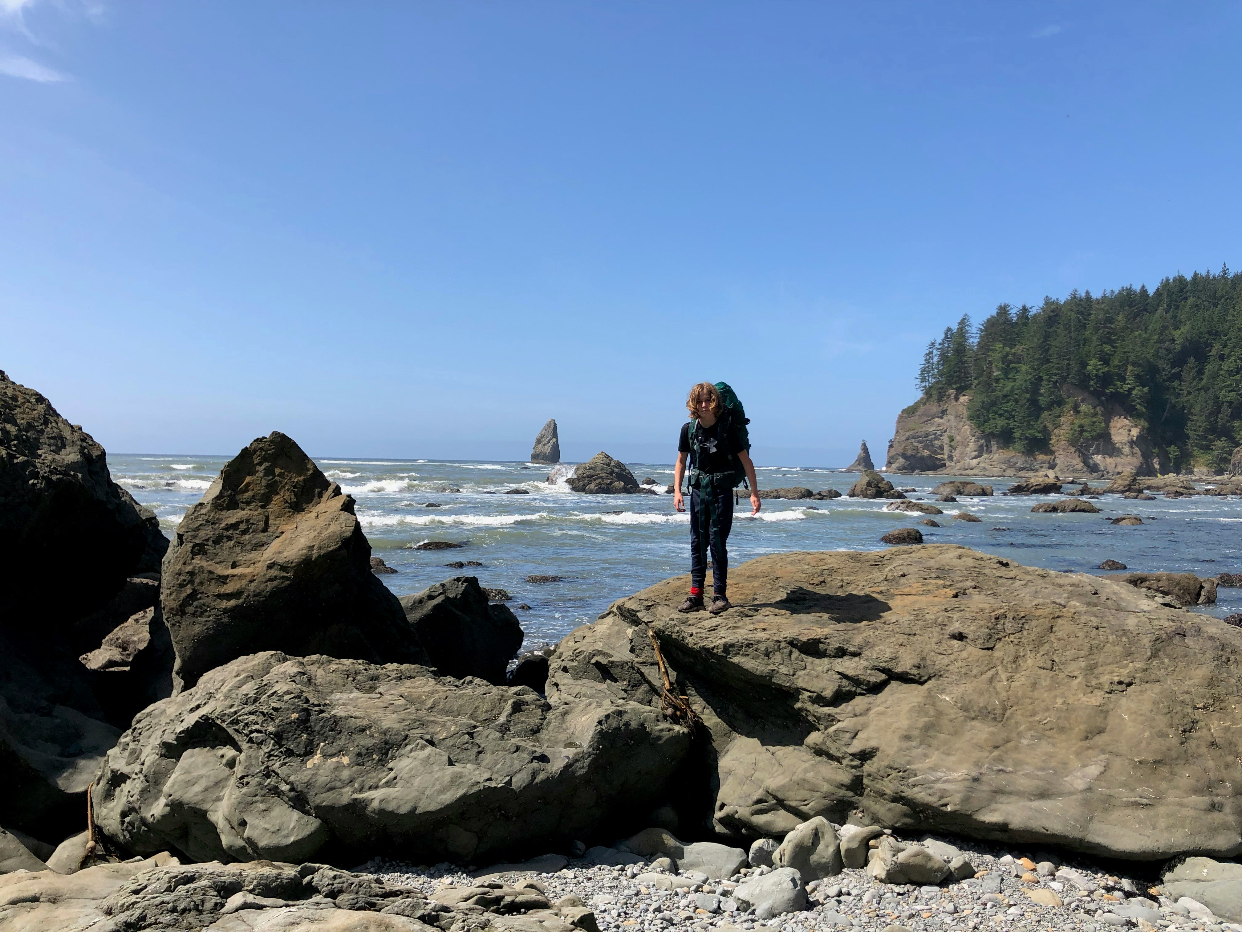 woman in black dress standing on rock formation near body of water during daytime