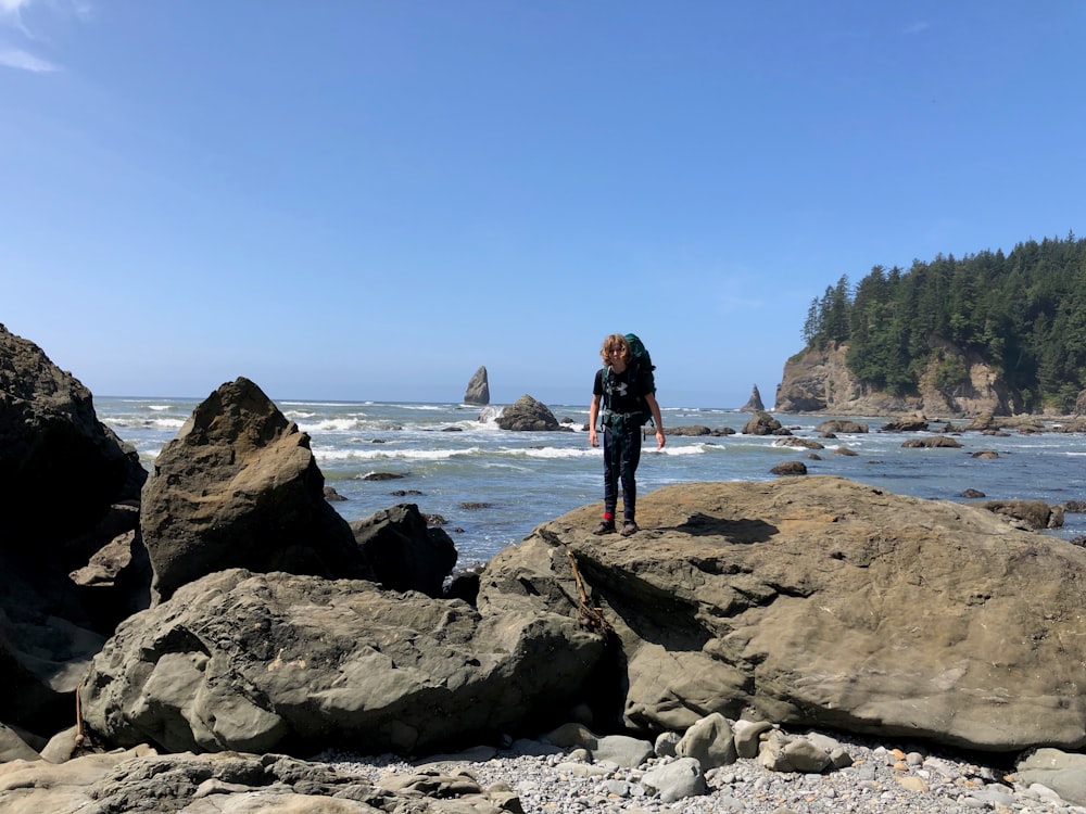 woman in black dress standing on rock formation near body of water during daytime