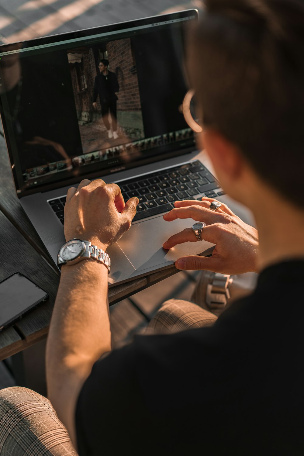 person wearing silver link bracelet round analog watch using black laptop computer