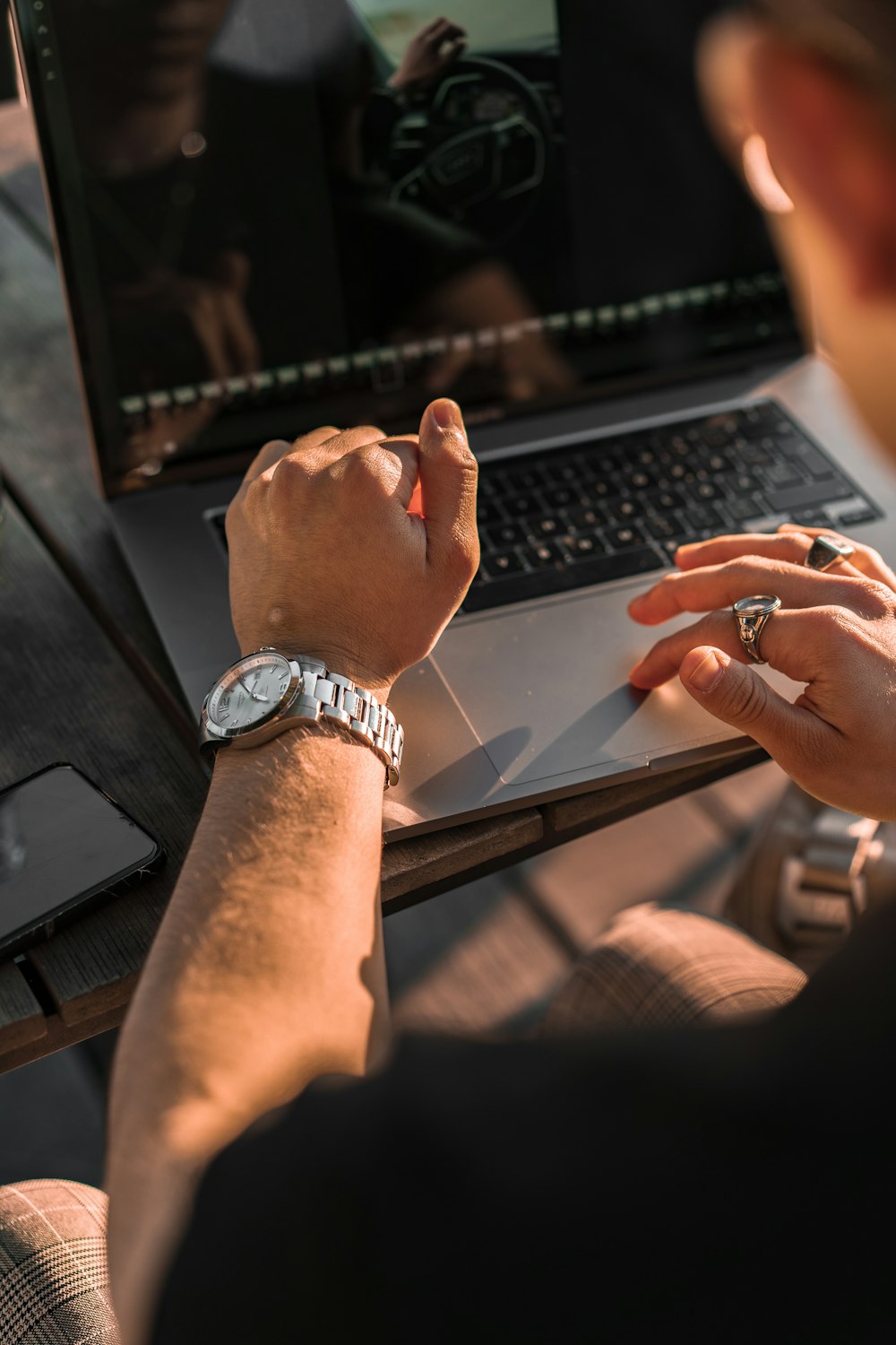 person wearing silver link bracelet round analog watch using macbook pro