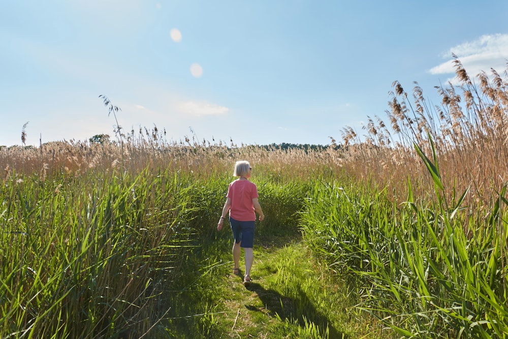 woman in blue long sleeve shirt and blue denim jeans walking on green grass field during