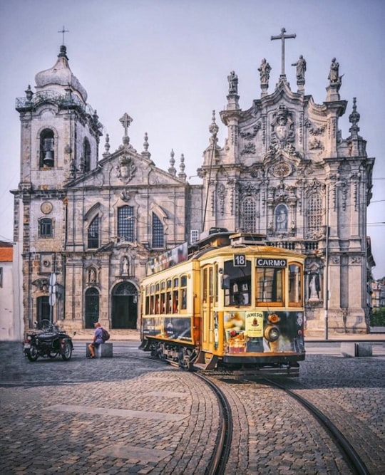 yellow tram in front of gray concrete building in Igreja do Carmo Portugal