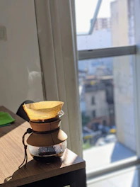 A sleek portable electric coffee maker on a wooden table with morning sunlight coming through a window