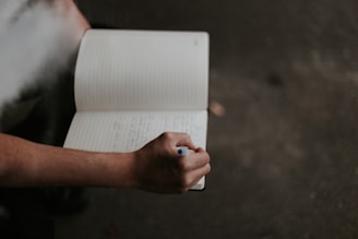 Person holding a notebook and a pen, thinking of what to write