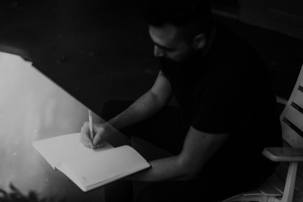 man in black t-shirt writing on white paper