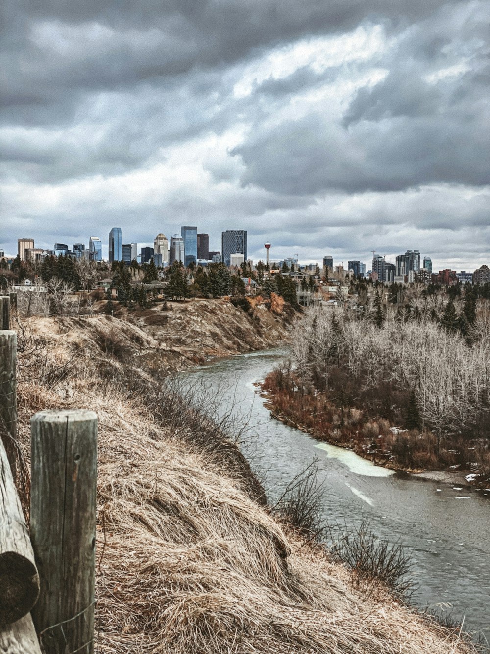 body of water between brown grass field near city buildings under white cloudy sky during daytime