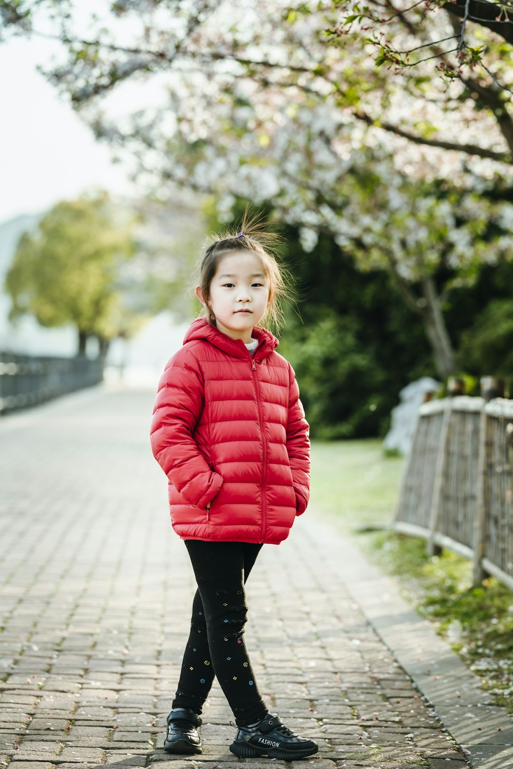 낮 동안 회색 콘크리트 통로에 서 있는 빨간 까마귀를 입은 소녀