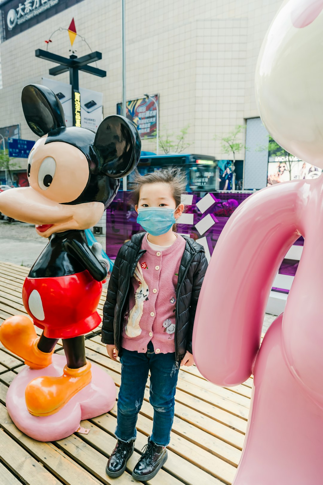 girl in pink jacket standing beside mickey mouse statue during daytime