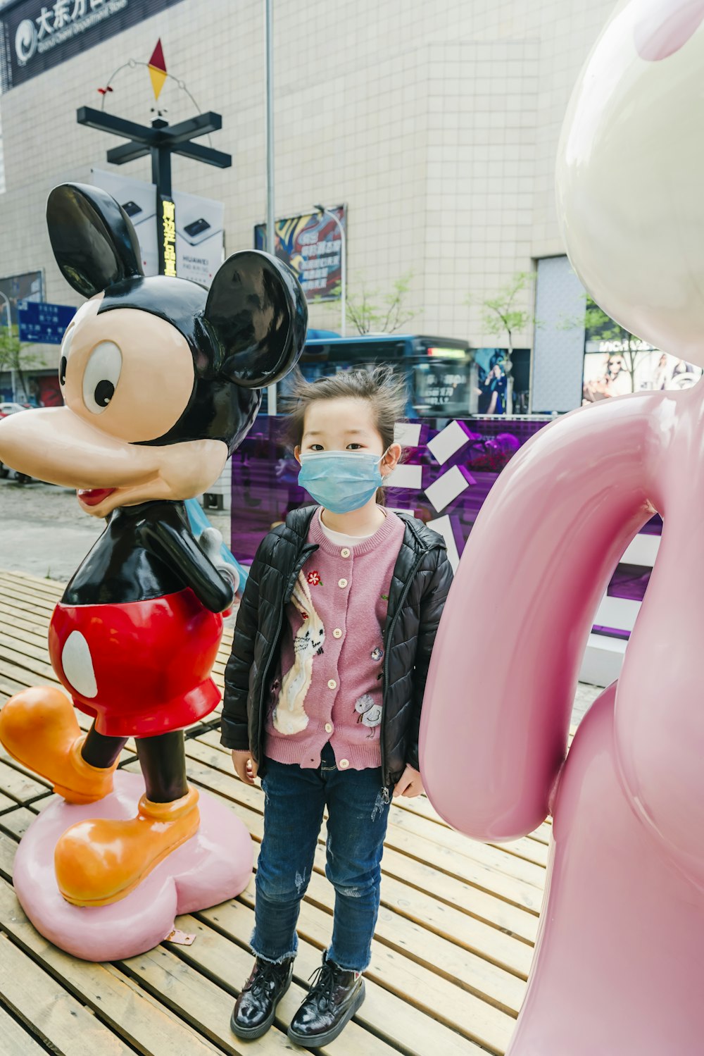 girl in pink jacket standing beside mickey mouse statue during daytime