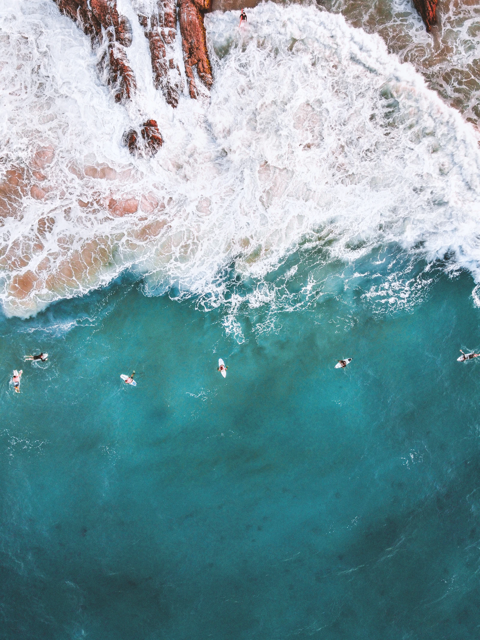 Aerial view of surfers and ocean waves beside a sandy coast.