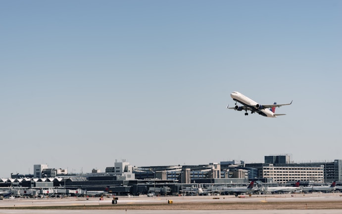 An airplane taking off with cargo containers visible on the tarmac below.