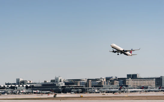 Modern airplane taking off with a clear blue sky and São Paulo cityscape in the background.