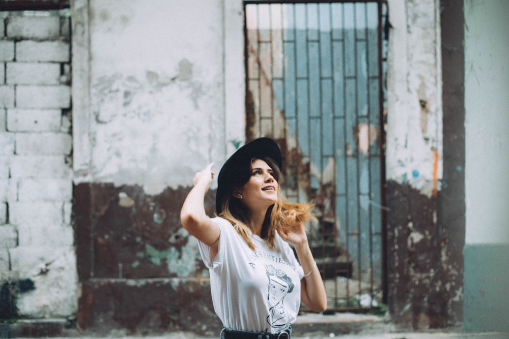 Mujer con camiseta blanca y gorro de punto negro de pie cerca de la pared