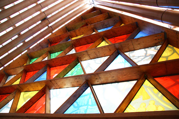 Colorful stained glass panel glowing warmly in natural light by a wooden frame.