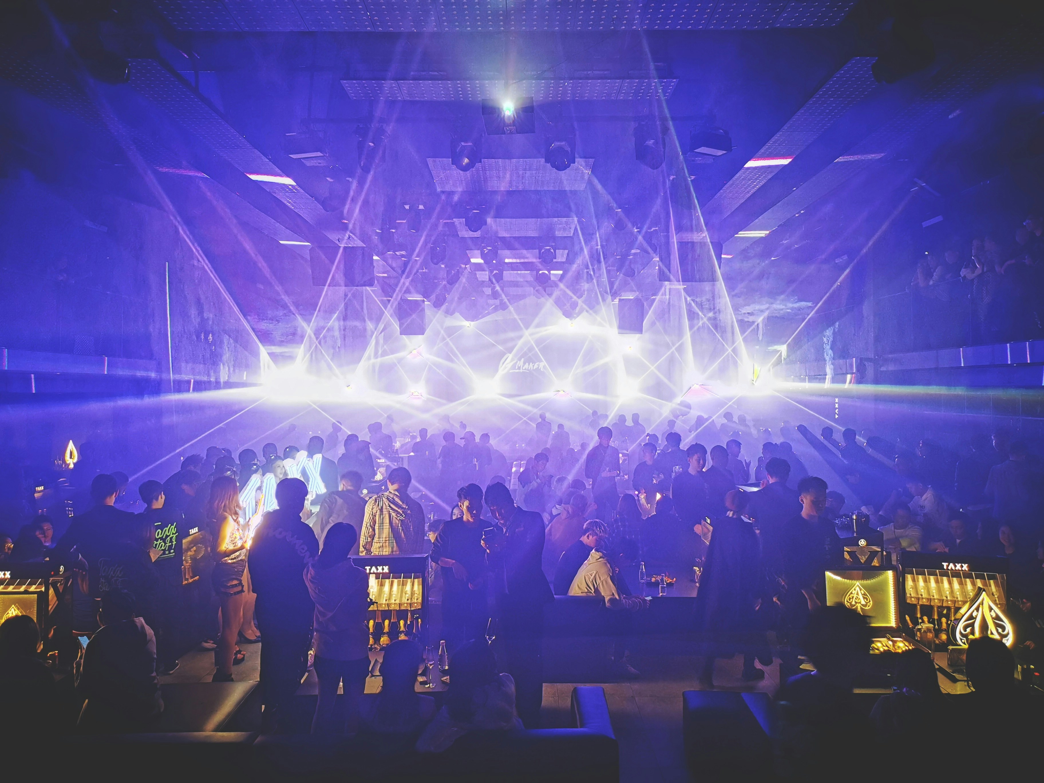 Packed dancefloor with laser beams and colourful LED lighting, crowd dancing, dark club atmosphere