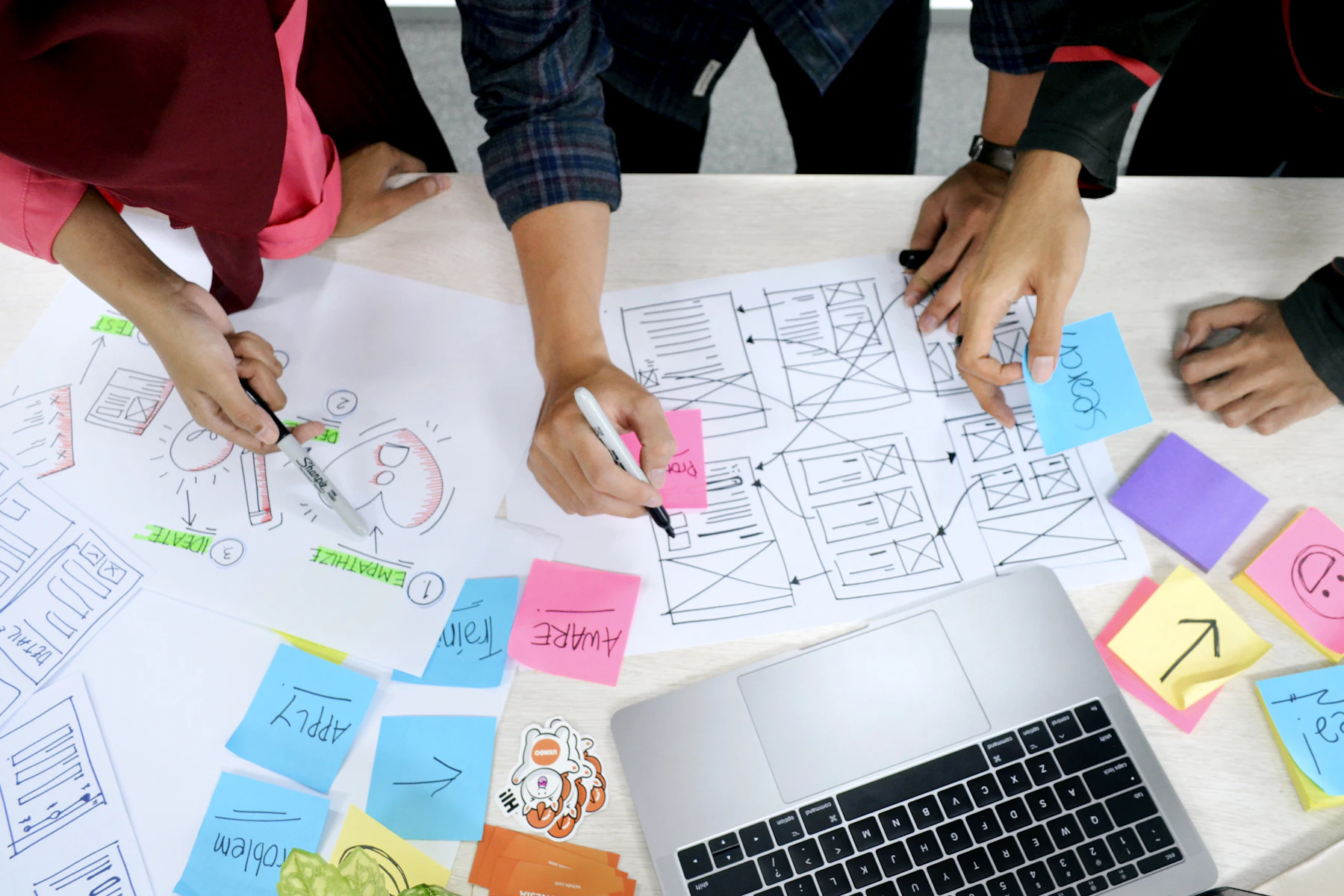 Team sketching layouts and structure by hand around a laptop