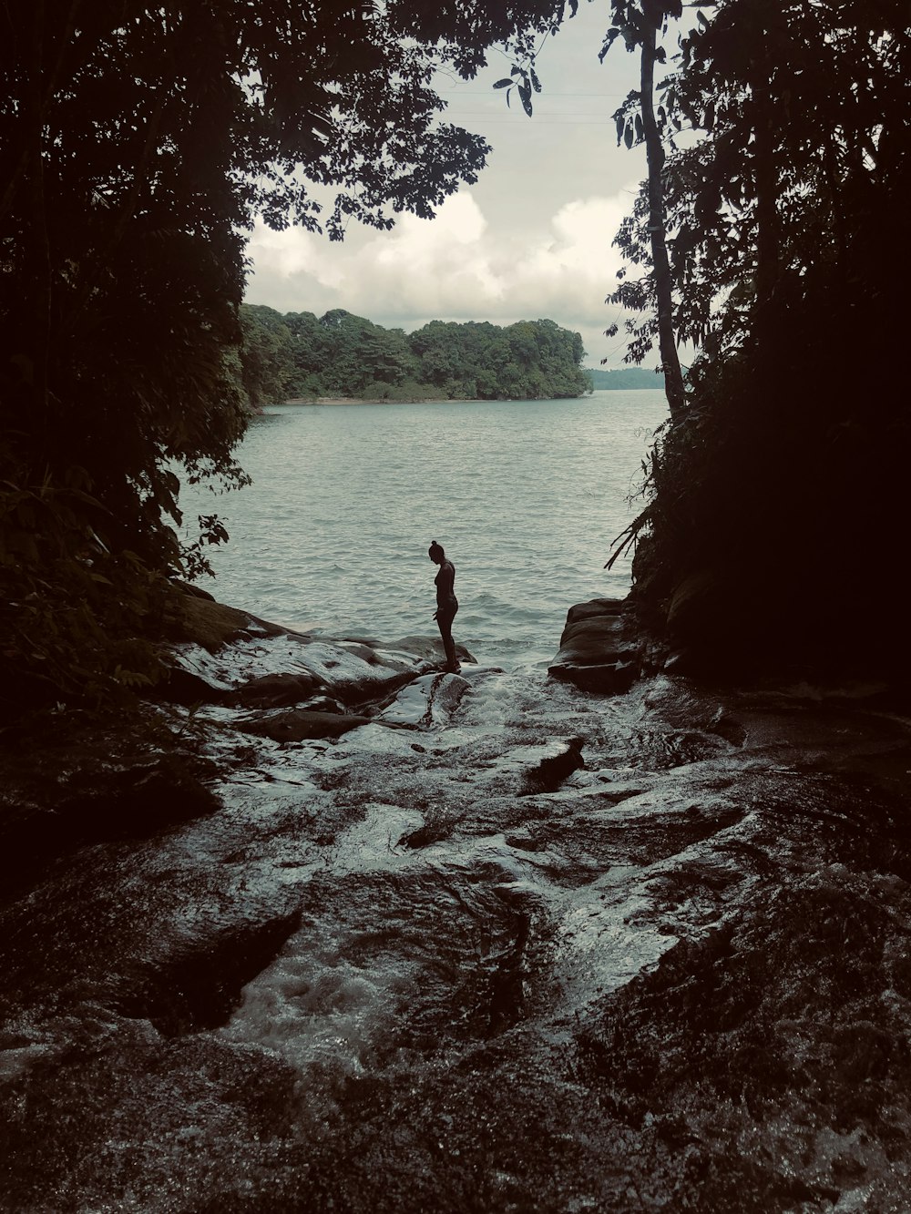 woman in black bikini standing on rock in the middle of body of water during daytime