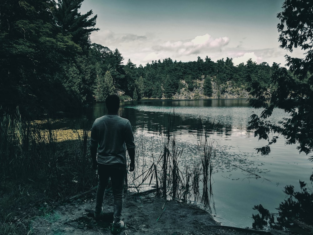 man in gray jacket standing on green grass near body of water during daytime