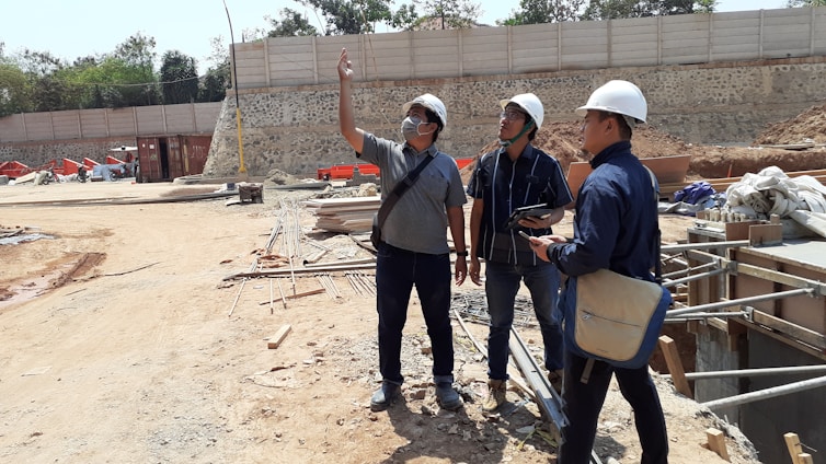 Three professionals reviewing construction plans at a busy heavy infrastructure site.