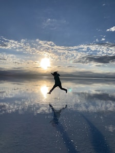 woman in black jacket and pants jumping on snow covered ground under blue and white cloudy