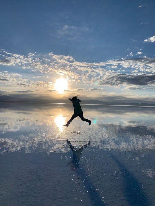 woman in black jacket and pants jumping on snow covered ground under blue and white cloudy in Salar de Uyuni Bolivia
