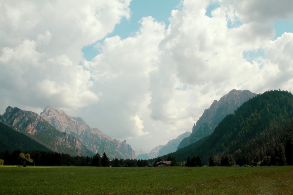 green grass field near green trees and mountains under white clouds and blue sky during daytime