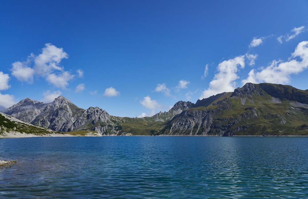 green and brown mountain beside body of water under blue sky during daytime