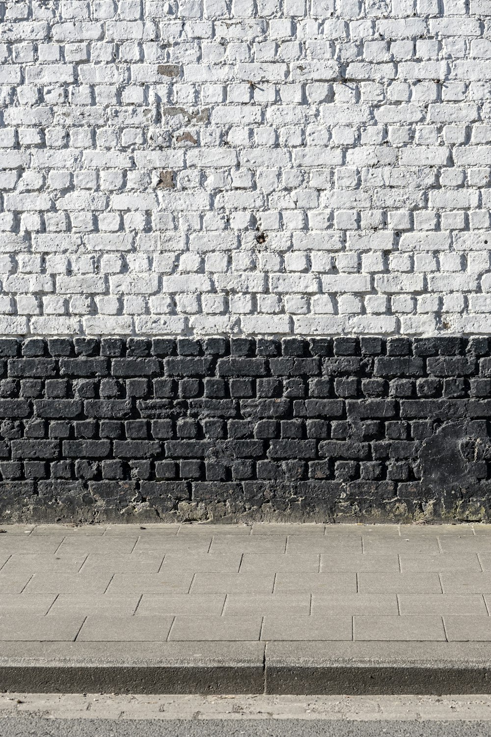 a man walking down a sidewalk next to a white brick wall