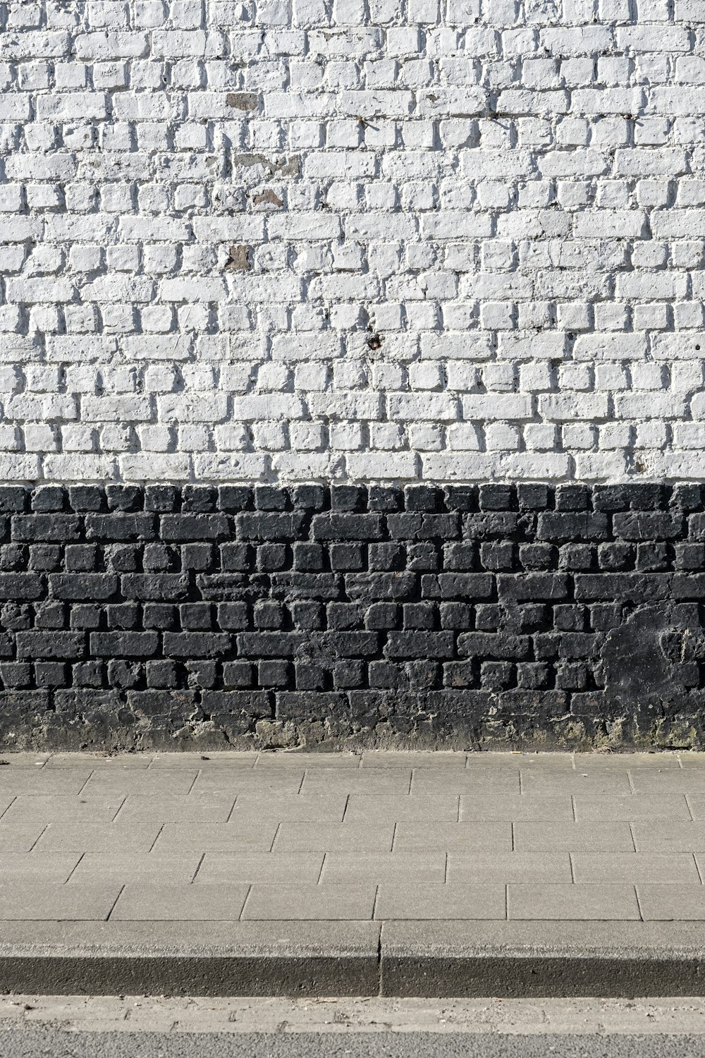 Un hombre caminando por una acera junto a una pared de ladrillo blanco