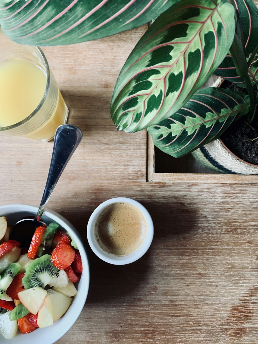 clear drinking glass with yellow liquid beside sliced strawberries and sliced lemon on brown wooden chopping