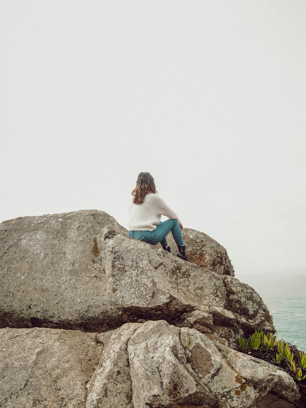 woman in blue tank top and blue denim jeans sitting on brown rock formation during daytime