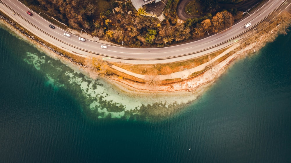 aerial view of white and brown road beside green body of water during daytime