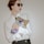 A person with red lipstick wearing sunglasses and a white shirt is holding a fashion magazine against a neutral background. The magazine cover features a portrait and the word 'VOGUE' in large letters.